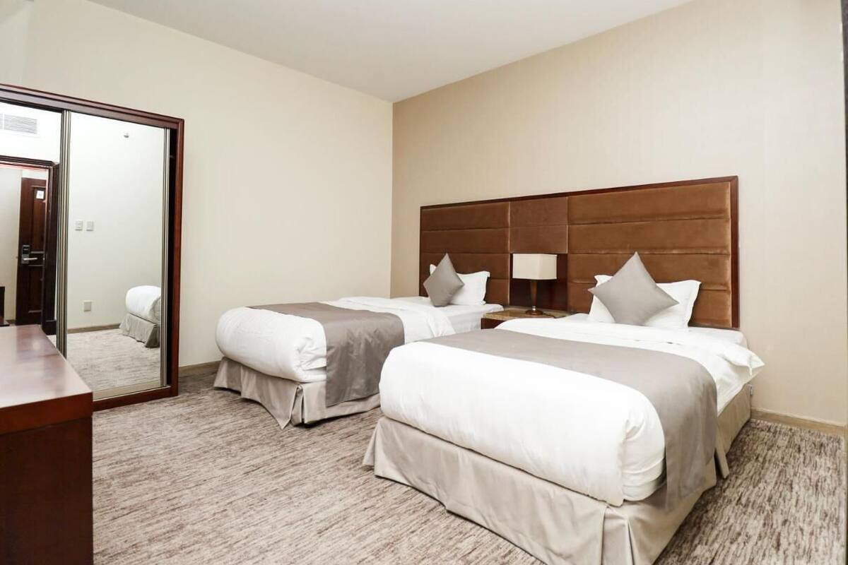 Een hotelkamer met twee bedden, een grote spiegel, een houten hoofdeinde en een vloerbedekking.