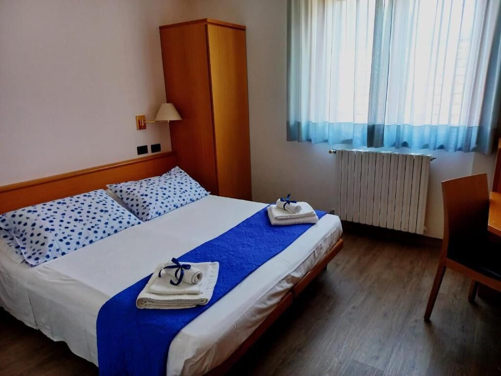 Une chambre d’hôtel avec un lit, une armoire, un bureau et une fenêtre avec des rideaux.