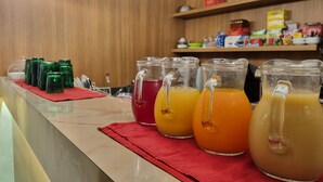 A counter with three pitchers of different colored beverages, a red cloth, and a wooden wall with shelves in the background. - Hotel La Ruota (Morbegno)