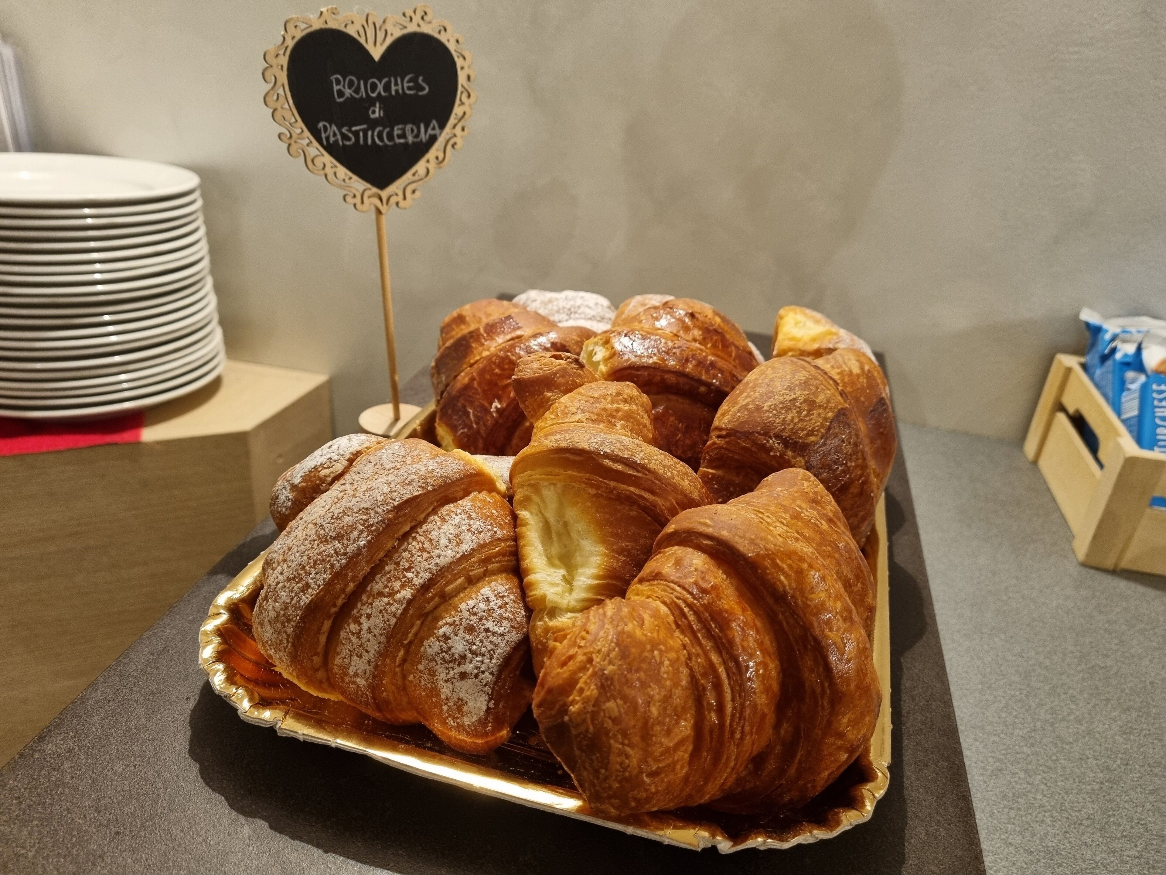 A tray of freshly baked croissants on a table with a sign that reads "Brioche di Pasticceria".