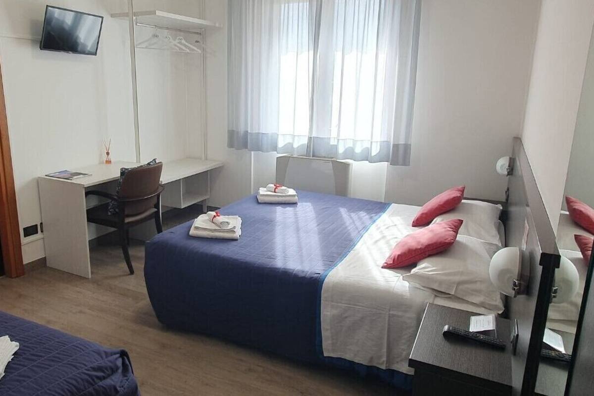 A hotel room with two beds, a desk, a chair, a TV, and a window with curtains.