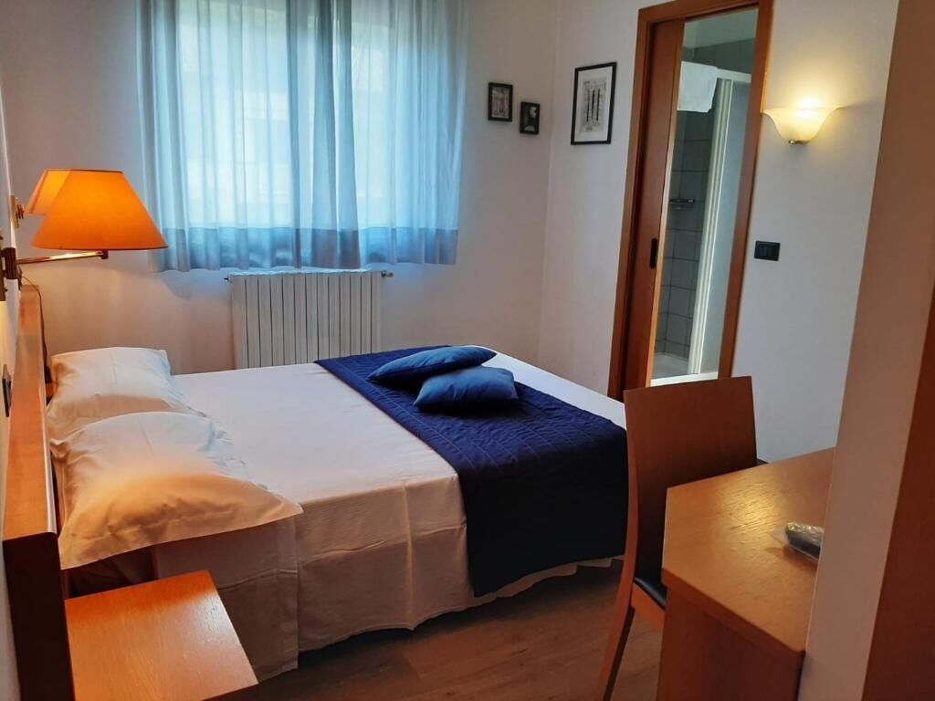 A bedroom with a bed, bedside table, lamp, and a view of a window with curtains.