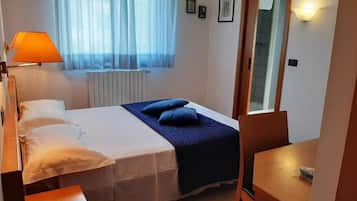 A bedroom with a bed, bedside table, lamp, and a view of a window with curtains.