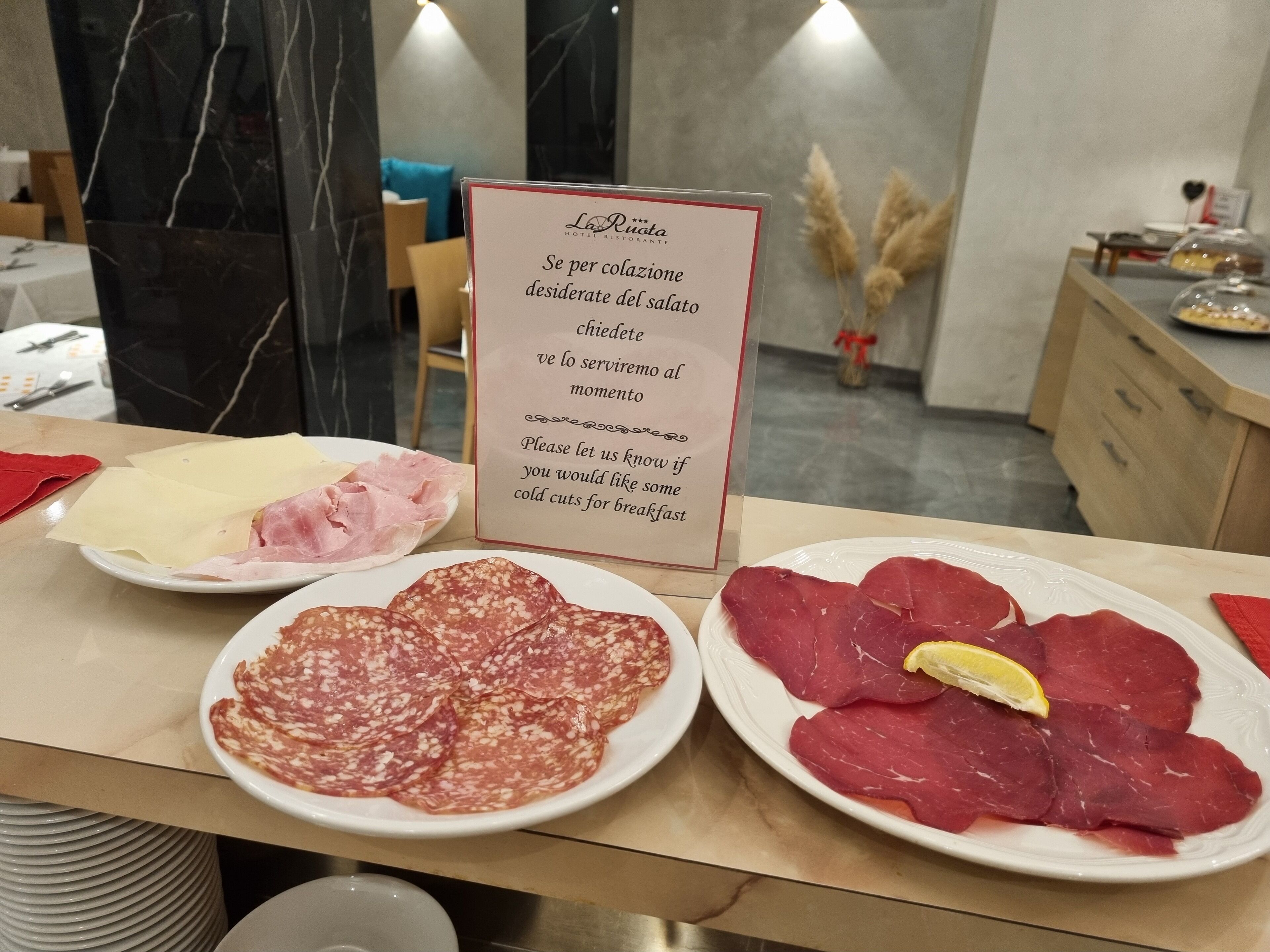 A hotel breakfast buffet with various cold cuts and salami displayed on plates.