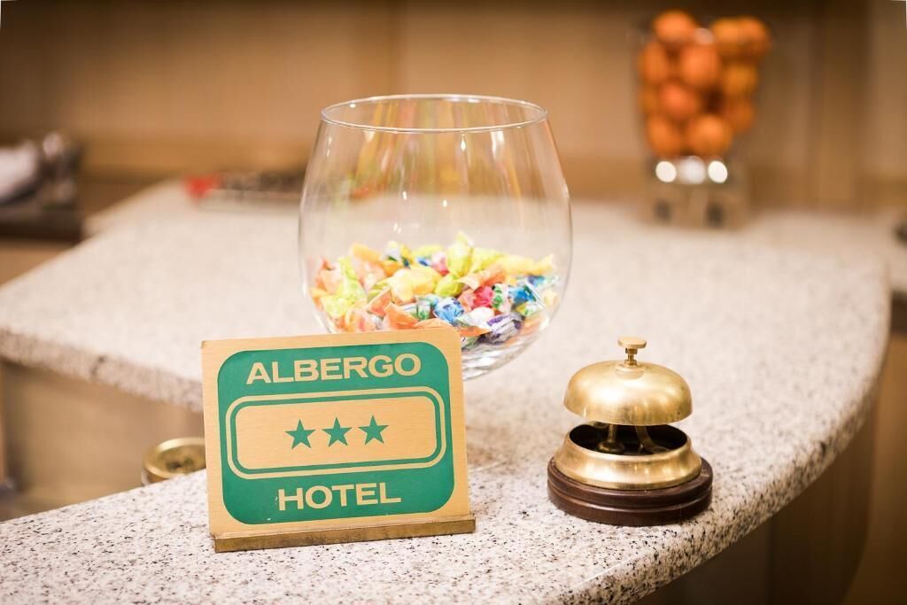 Cartell d'hotel amb una classificació de tres estrelles, un got amb caramels de colors i una campana sobre un taulell.