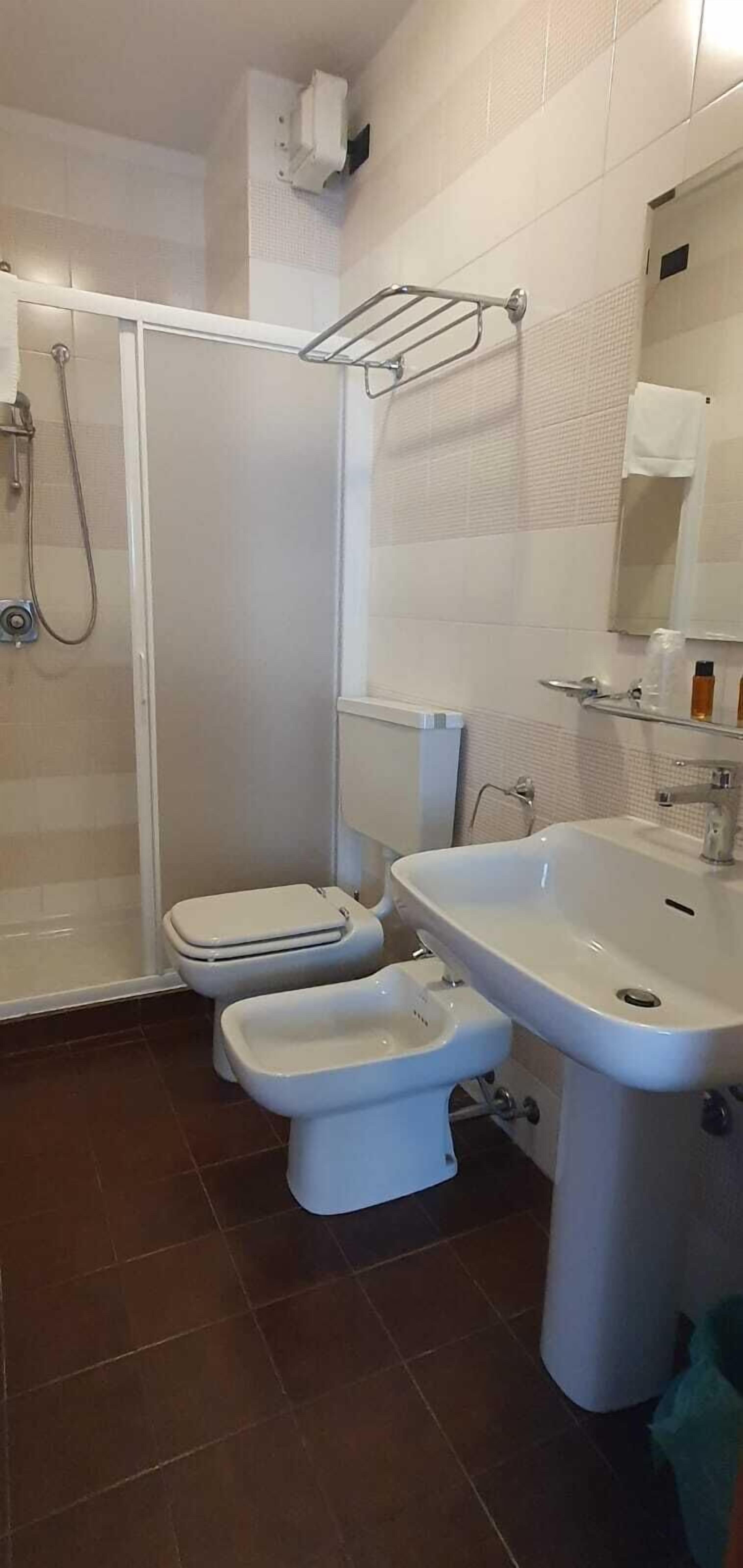 A bathroom with a shower, toilet, bidet, and sink.