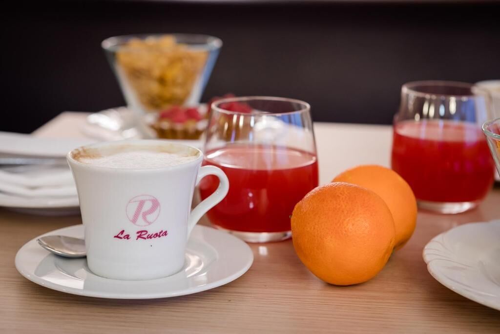 Una mesa con una taza blanca con la etiqueta "La Rusta", una bebida roja y dos naranjas.