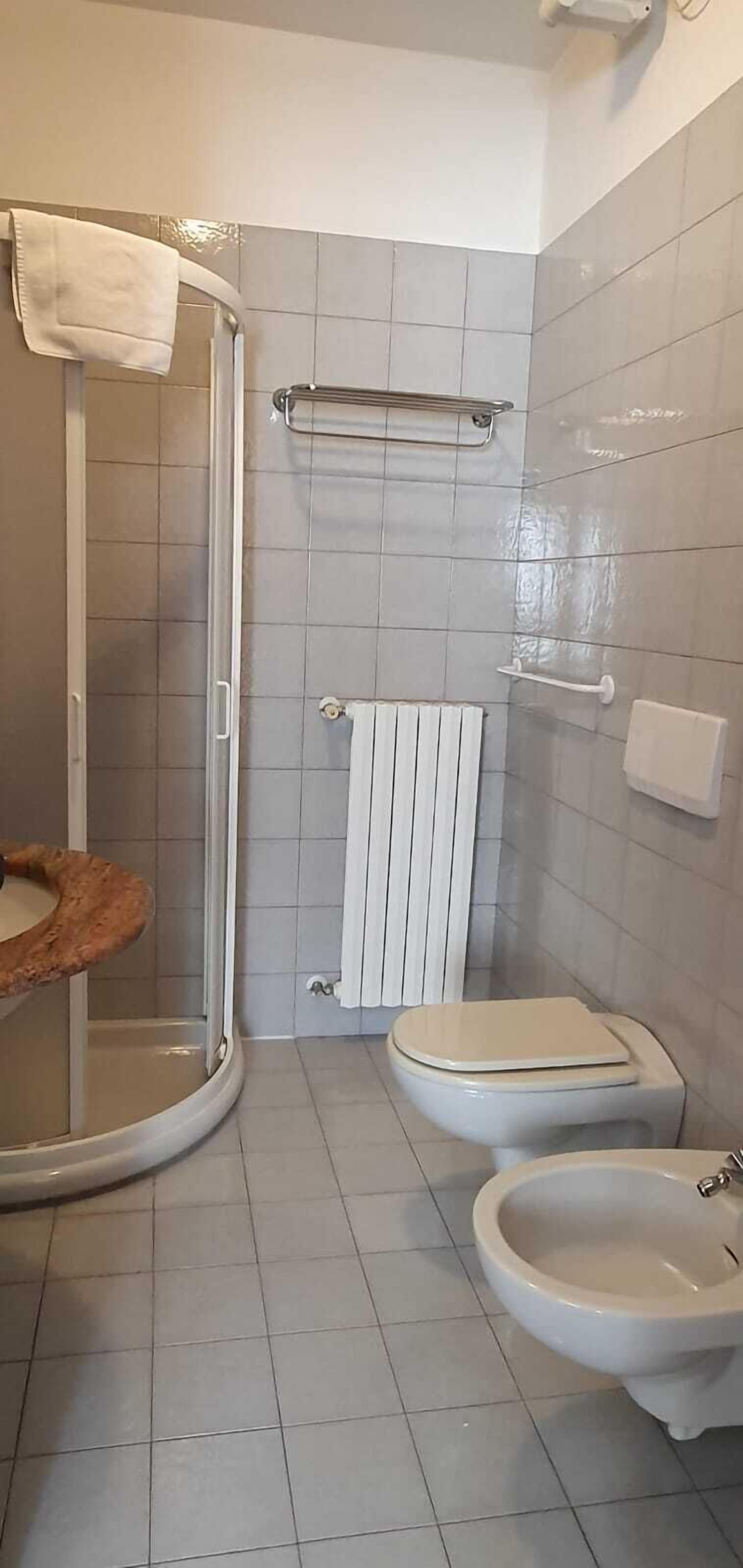 Een badkamer met douche, toilet, bidet en een handdoekhouder.