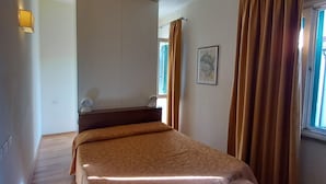 A bedroom with a bed, a bedside table, a lamp, a window with curtains, and a wall-mounted light fixture.