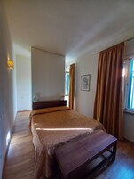 Un dormitorio con cama, mesita de noche, lámpara, ventana con cortinas e iluminación en la pared.