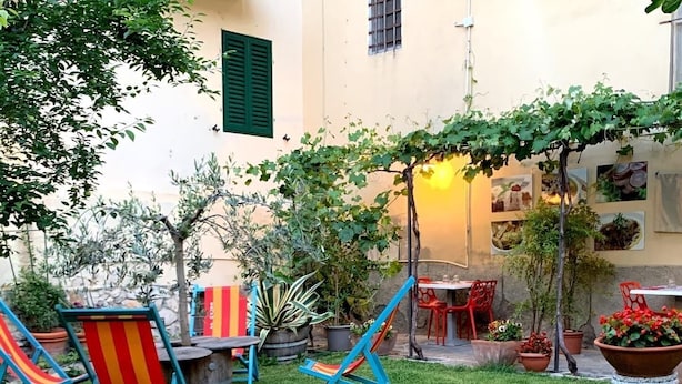 A well-maintained outdoor patio area with a grassy lawn, two blue and red striped lounge chairs, a small table with chairs, and a variety of potted plants.