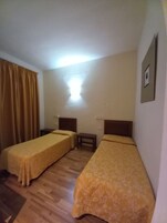 Habitación de hotel con dos camas individuales, una mesita pequeña y una lámpara fijada a la pared.