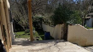 Un patio con suelo de baldosas, una estructura de madera a la izquierda y un jardín al fondo.