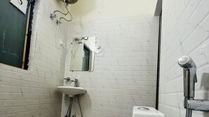 A small, compact bathroom with a white toilet, a sink, and a shower. - Badal Inn (New Delhi)