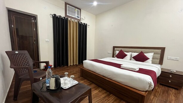 A hotel room with a wooden bed, a desk with a kettle and cups, and a chair. - Badal Inn (New Delhi)