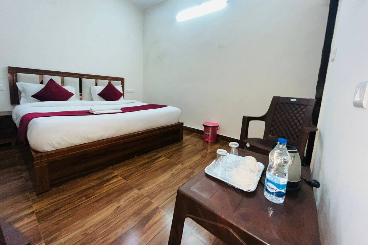 A hotel room with a wooden bed, white walls, a small table with a water bottle and a tray with cups.