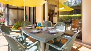 Een eetgedeelte met een tafel voor vier personen, omringd door stoelen, en overdekt met gele parasols.
