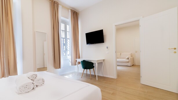 A hotel room with a bed, a desk, a TV, and a view of the outside. - Charme & Chic Nazionale (Rome)