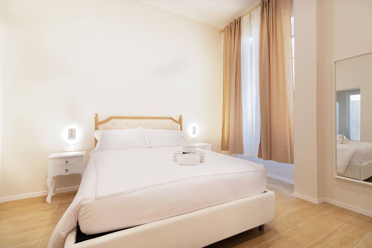 A neatly arranged bedroom with a large bed, bedside tables, and a mirror.