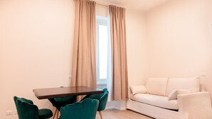 A modern living room with a beige sofa, a wooden dining table with teal chairs, and beige curtains. - Charme & Chic Nazionale (Rome)