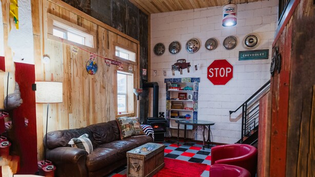Una sala de estar acogedora con un sofá de cuero marrón, un tapete rojo y negro a cuadros y una señal de stop roja en la pared.