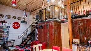 Interior de restaurante con techo de madera, una escalera, decoración rojo y blanco, y varios objetos antiguos en las paredes.