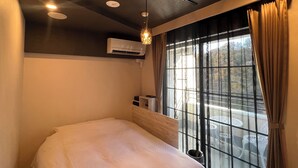 Une chambre à coucher comprenant un lit, un appareil de climatisation, une fenêtre avec des rideaux et des spots encastrés au plafond.