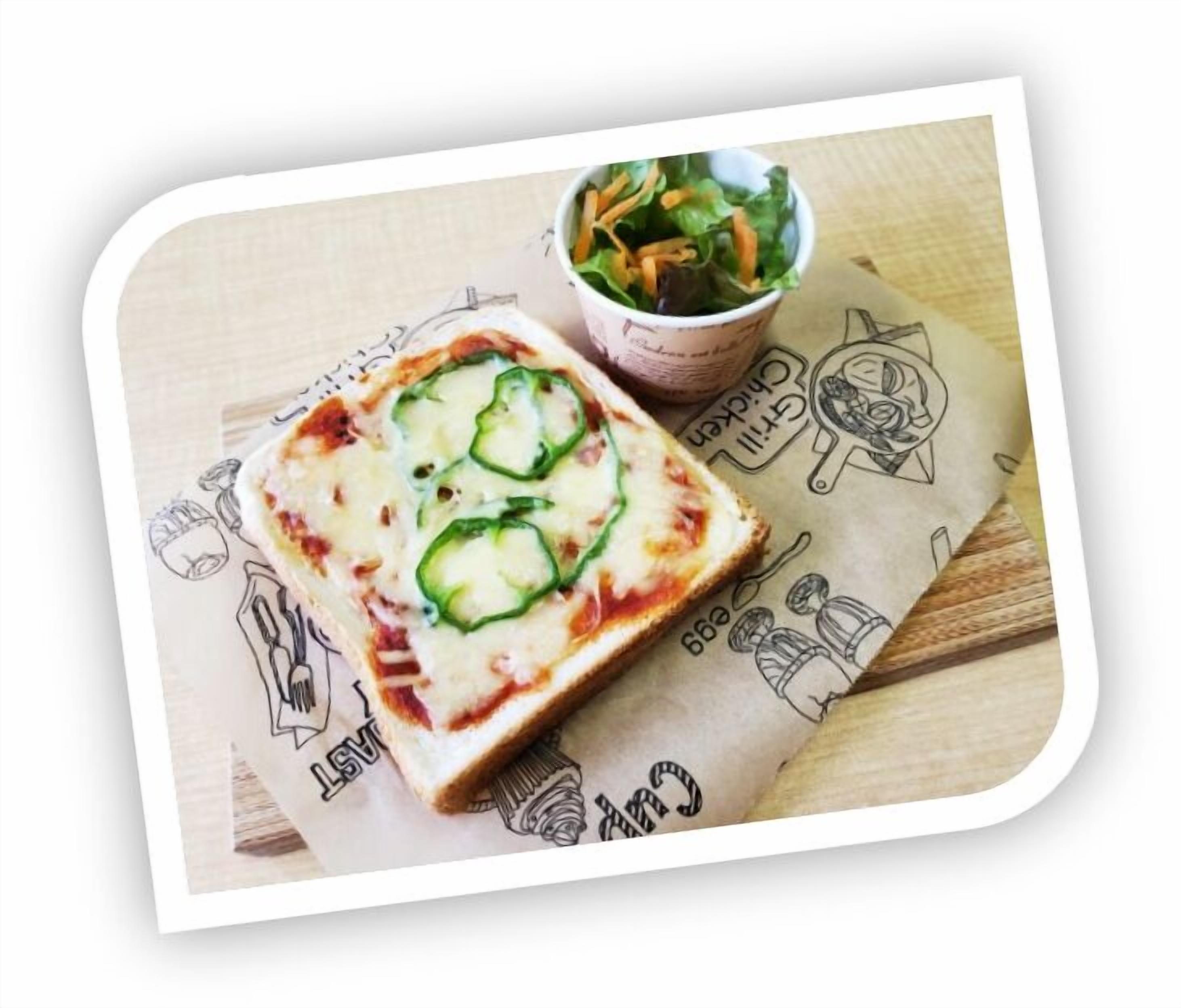 A pizza with green toppings on a wooden surface, a cup of salad, and a paper with illustrations.