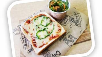 A pizza with green toppings on a wooden surface, a cup of salad, and a paper with illustrations.