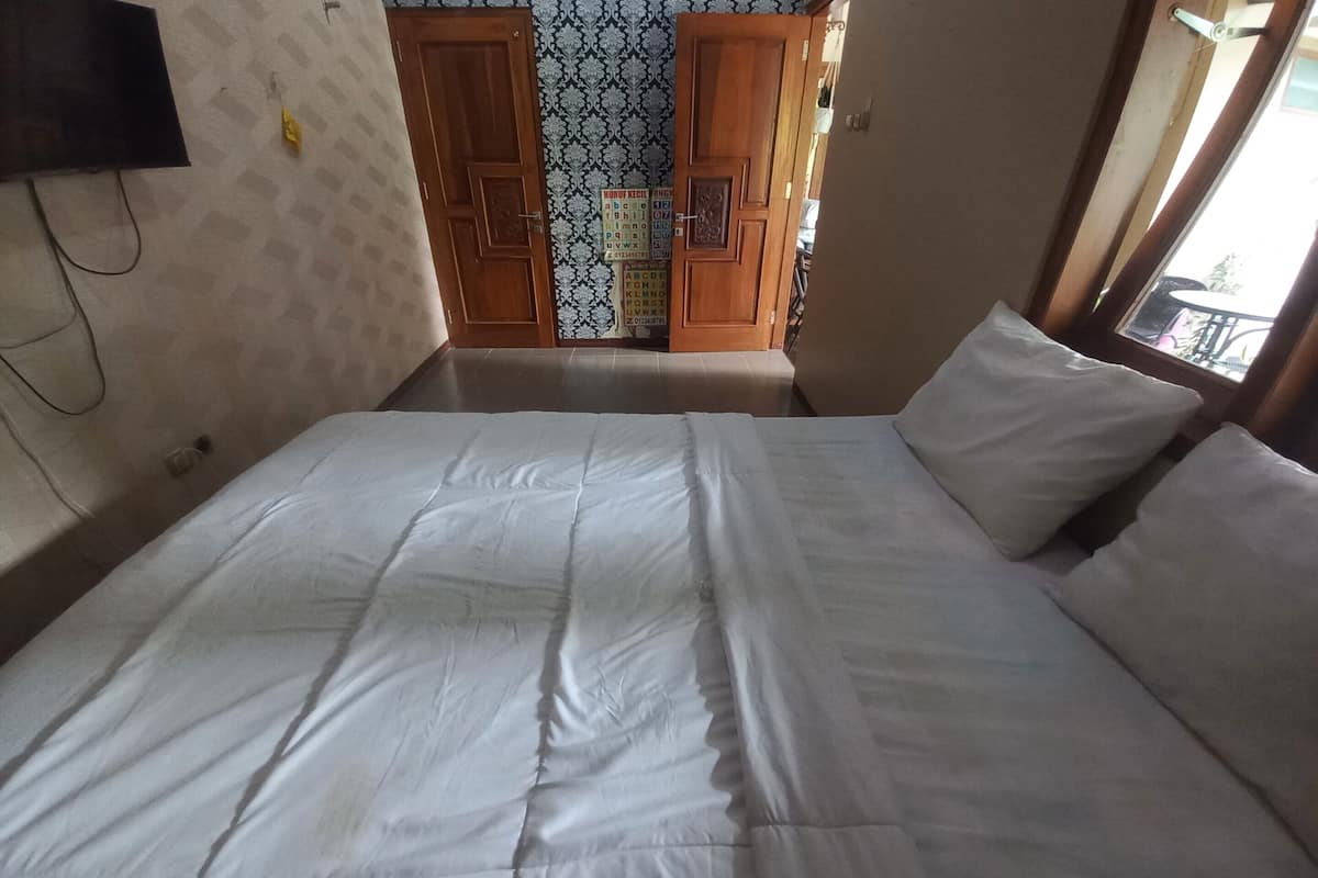 A bedroom with a large bed, wooden doors, a patterned wallpaper, and a window with a view.