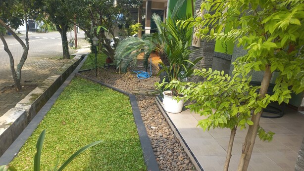 A landscaped garden with a grassy area, a pebble border, and various potted plants. - Hotel O Homestay Koe Syariah (Sukaradja)