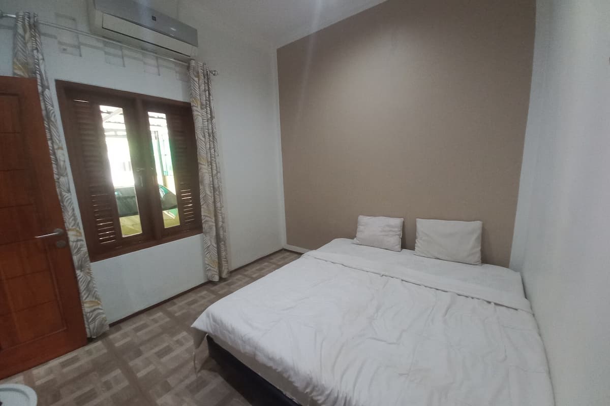 A bedroom with a bed, a window with curtains, and an air conditioning unit.