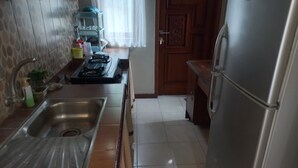 A kitchen with a stainless steel sink, a refrigerator, and a window with a curtain. - Hotel O Homestay Koe Syariah (Sukaradja)
