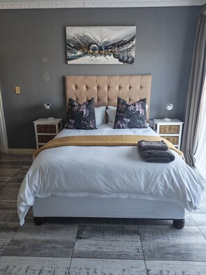 A neatly made bed with a tufted headboard, two bedside tables with lamps, and a large abstract painting above the bed. - Charming 3-bedroom bed & breakfast in tranquil East London (East London)