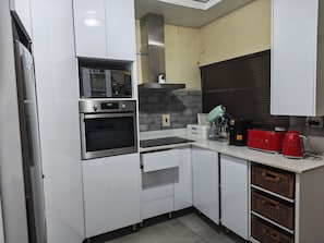 A modern kitchen with white cabinetry, a built-in oven, a microwave, a bread box, and a coffee maker. - Charming 3-bedroom bed & breakfast in tranquil East London (East London)