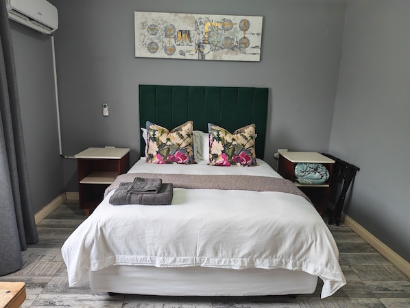 A hotel room with a bed, a headboard, a wall-mounted artwork, a bedside table, and a nightstand. - Charming 3-bedroom bed & breakfast in tranquil East London (East London)