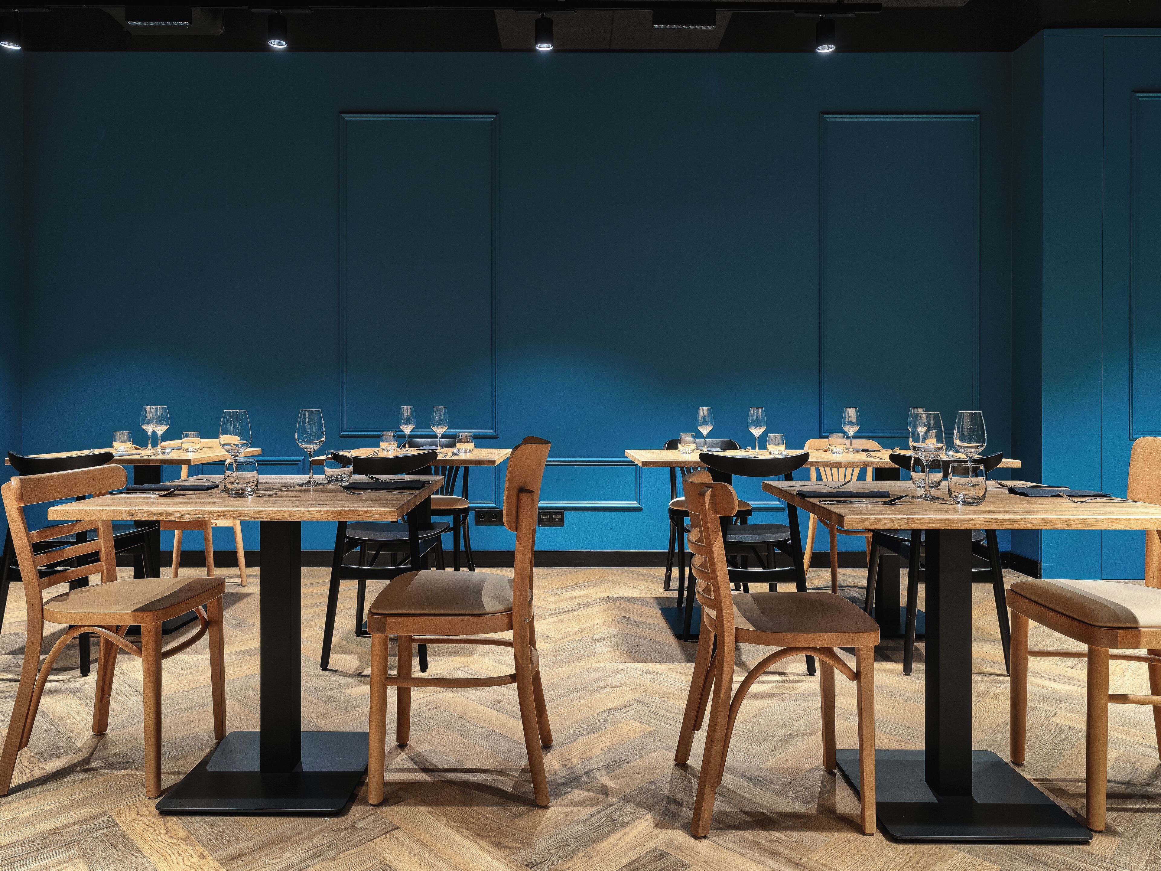 Een restaurant met houten tafels en stoelen, blauwe wanden en een glanzende houten vloer.