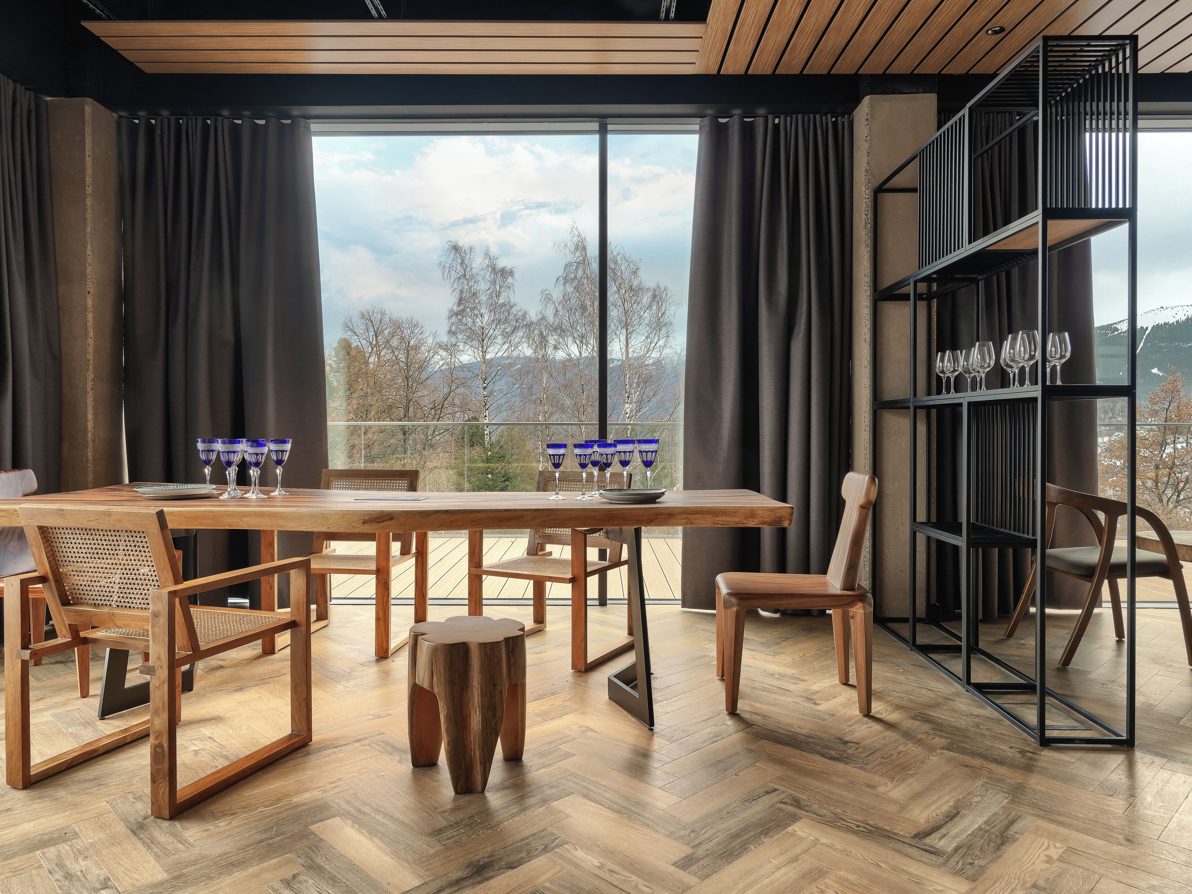 Un comedor moderno con una mesa de madera, sillas y una barandilla de vidrio con vistas a un paisaje pintoresco.