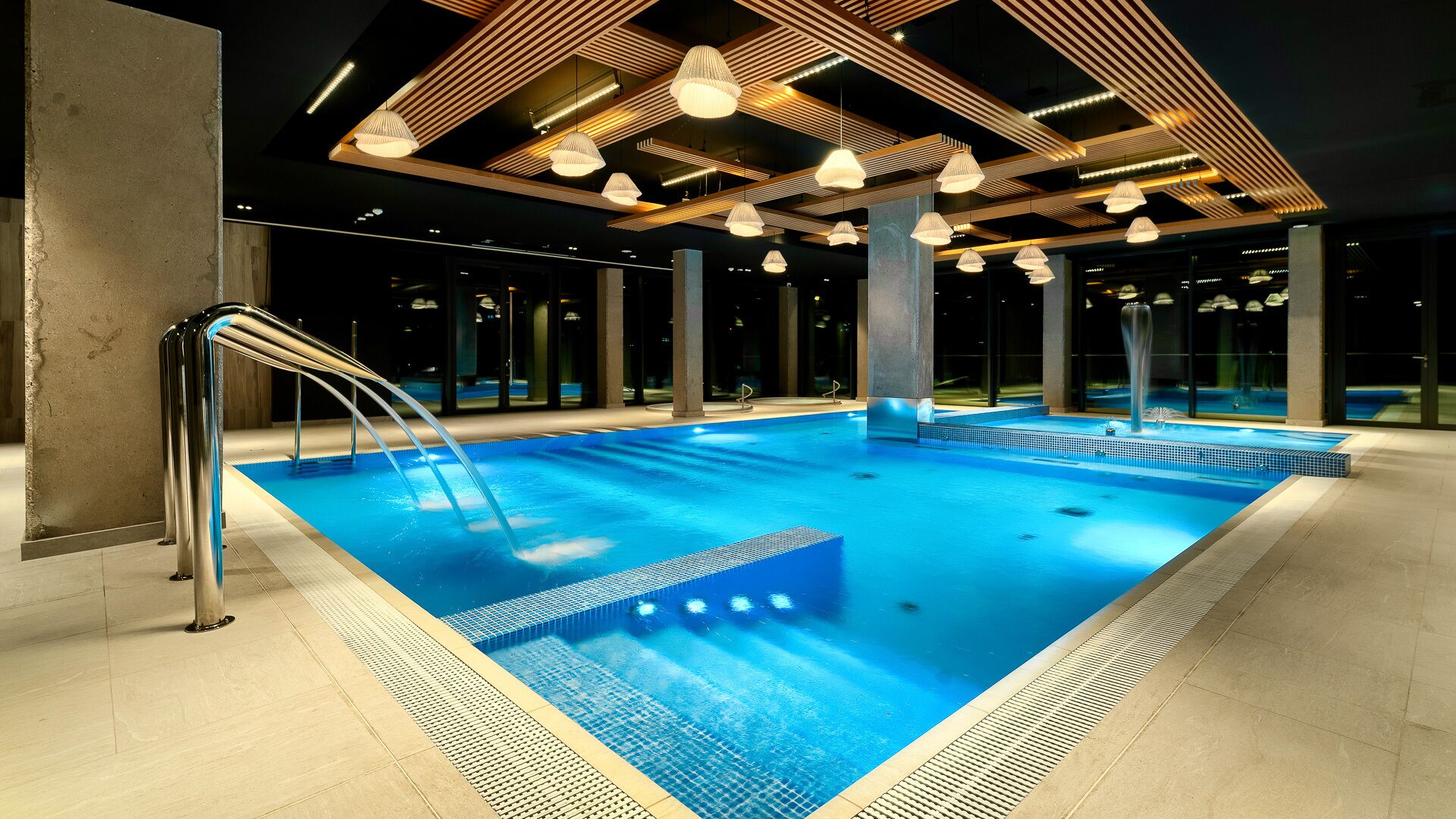 Une piscine intérieure moderne, dotée d’un système de filtration à eau claire, d’une échelle en métal et d’un éclairage contemporain.