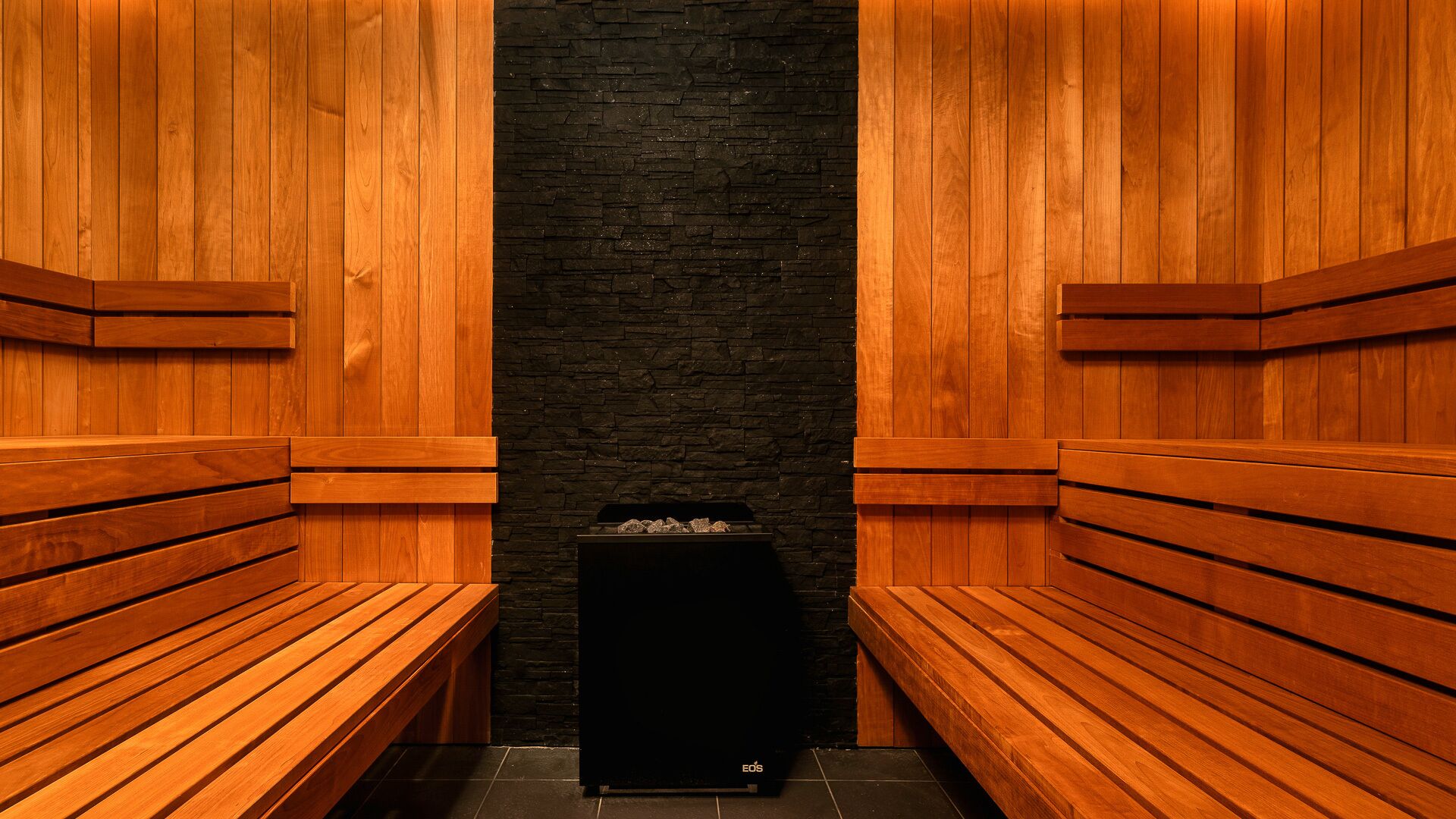 A sauna with wooden benches and a black stone wall.