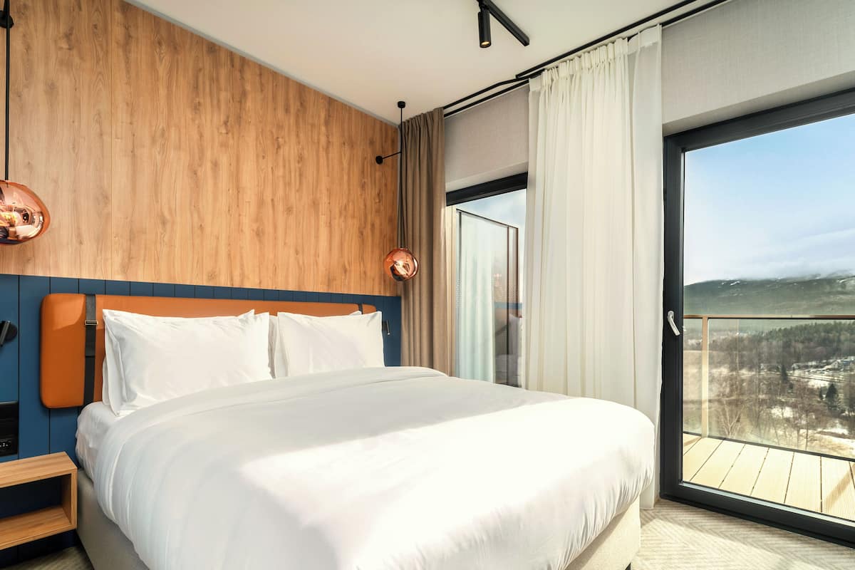 Ett modernt hotellrum med en stor säng, en väggpanel i trä och en balkong med en vacker utsikt.