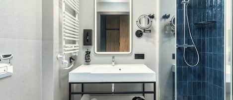 Un baño moderno con un lavamanos blanco, un espejo, un perchero para toallas, una ducha con puerta de vidrio y baldosas de suelo estampadas.