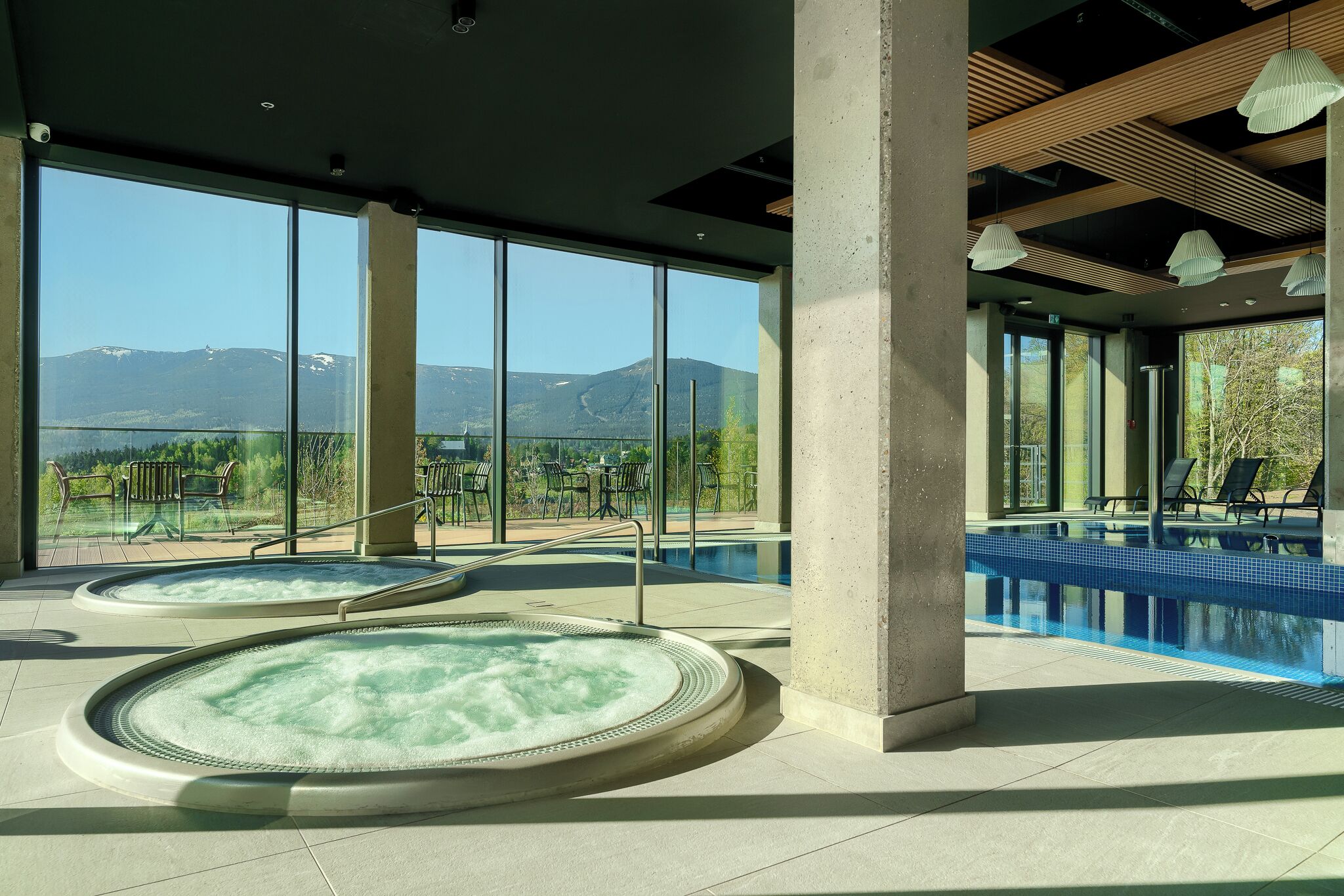 A spa area with two hot tubs and a pool, large windows offering mountain views.