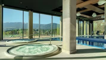 Zona de spa con dos jacuzzis y una piscina, con amplios ventanales que ofrecen vistas a la montaña.