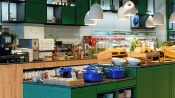Una cocina moderna con armarios verdes, una mesa de buffet con ollas azules, y lámparas colgantes.