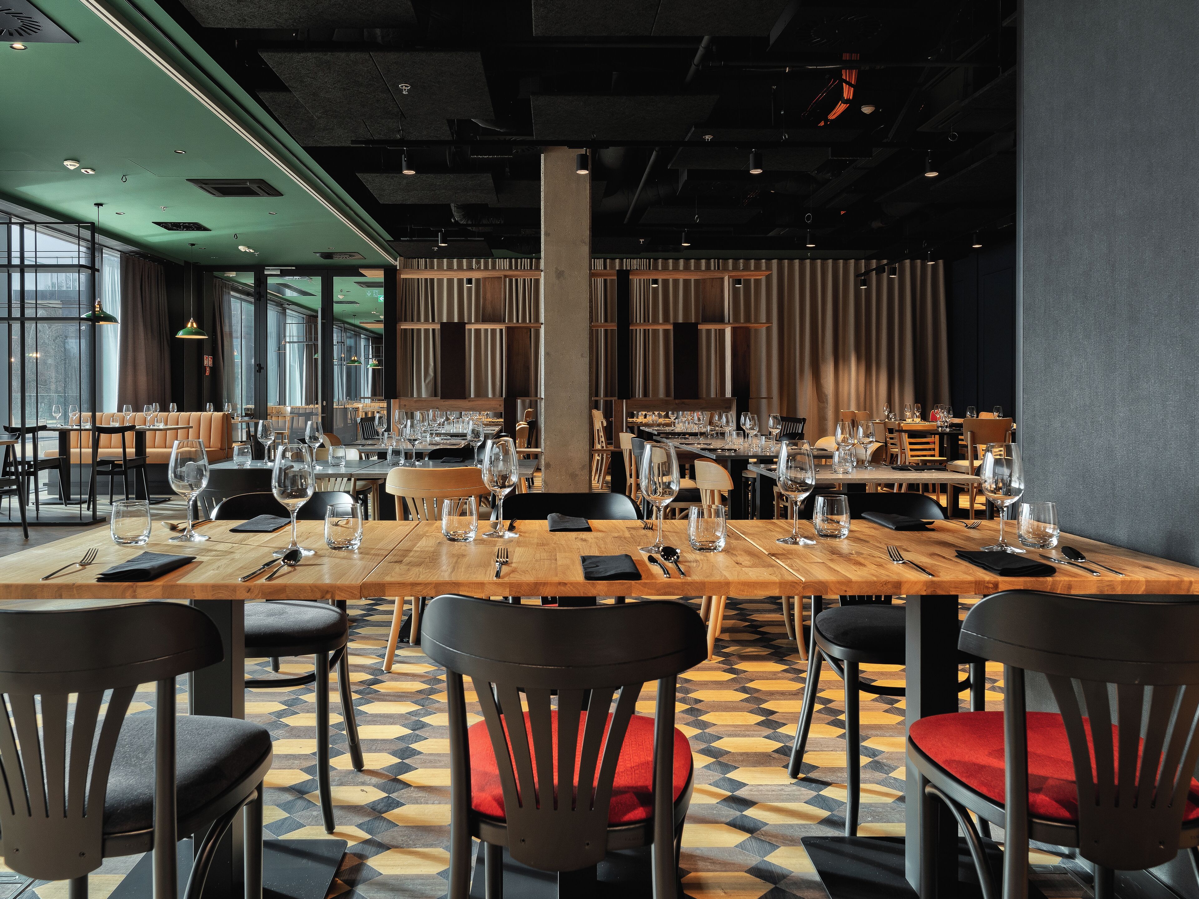 A restaurant with a long wooden table set for dining, surrounded by black chairs with red cushions.