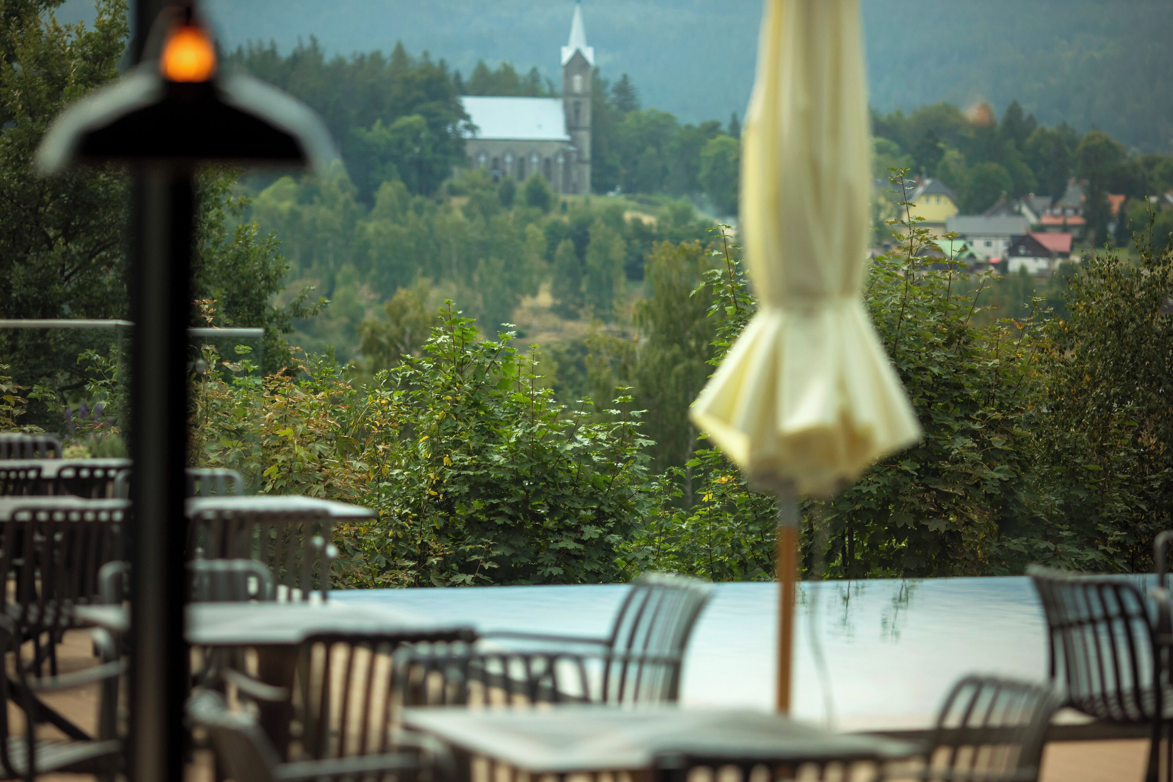 An outdoor seating area with tables and chairs, overlooking a church and a lake.
