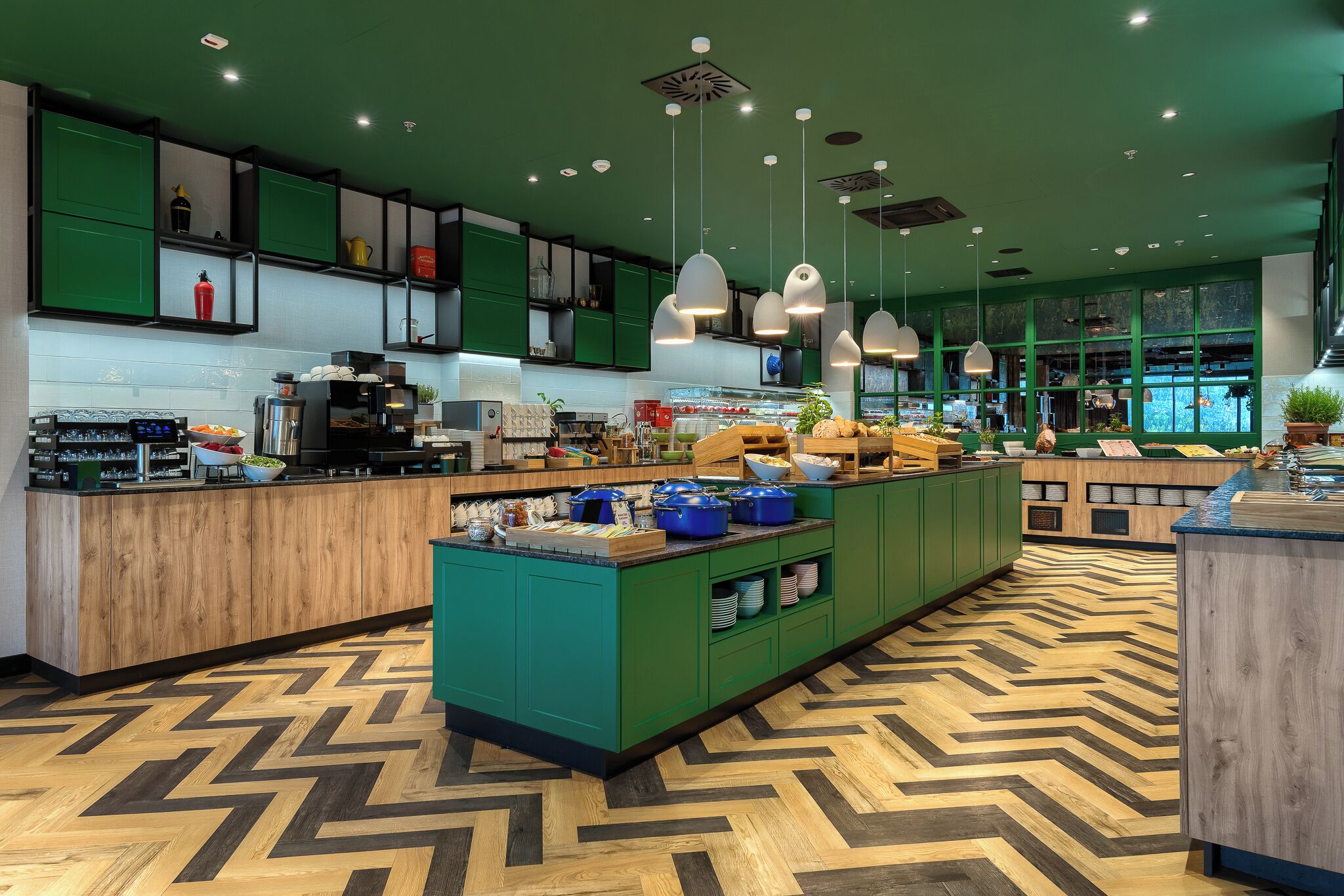 A modern kitchen with green cabinets, a central island with food items, and pendant lighting.