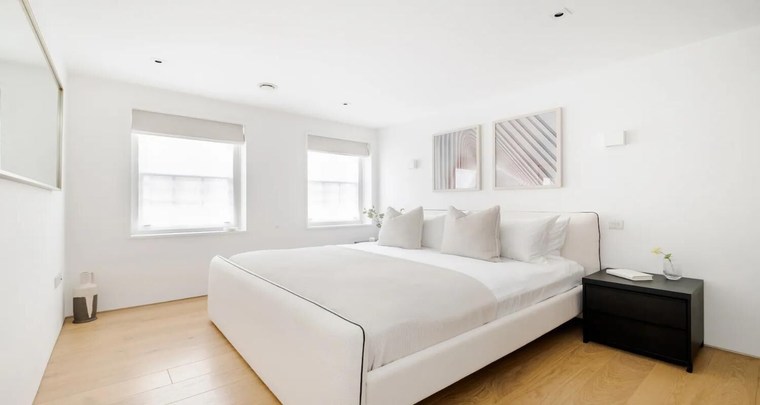 A modern bedroom with a large bed, two windows, a bedside table, and a nightstand.