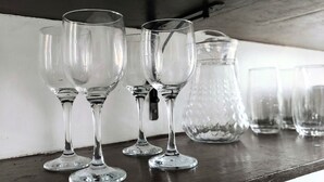 Une rangée de verres à vin transparents et une carafe en cristal sont posés sur une surface en bois.